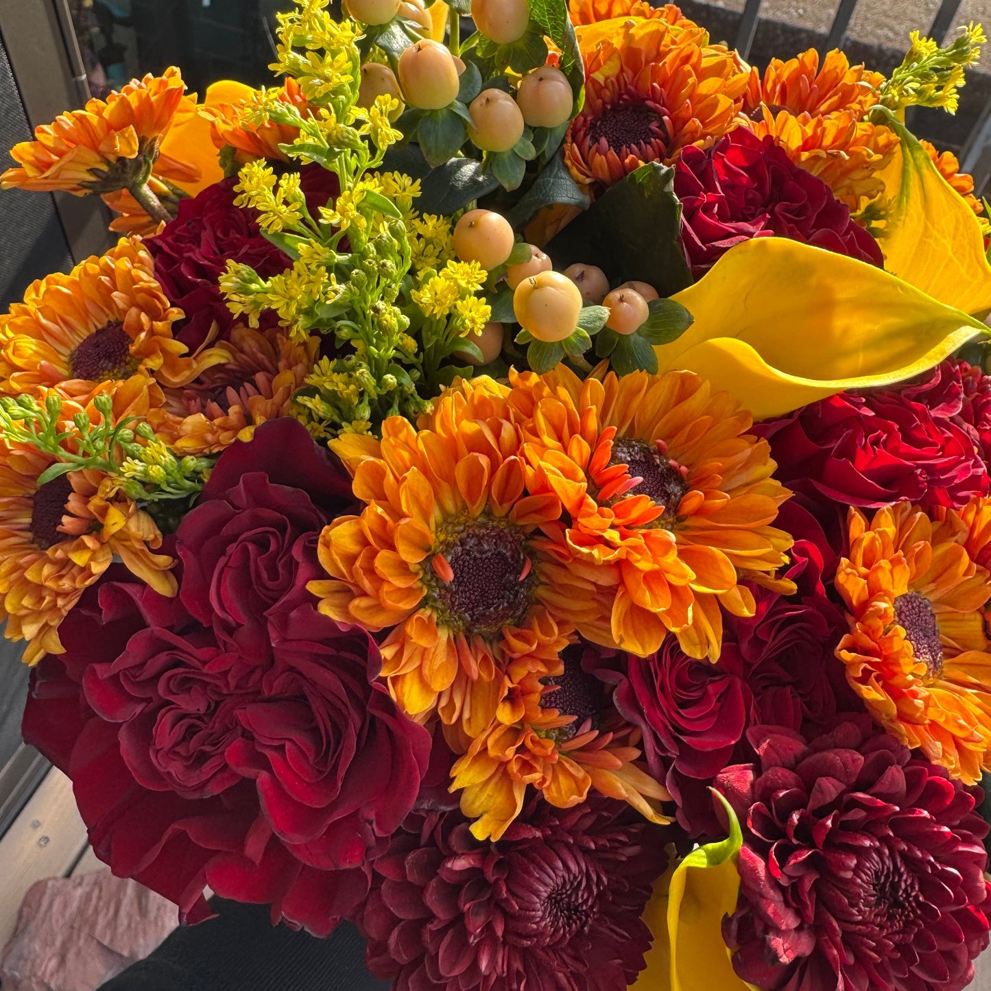 Bouquet of red, yellow, and orange flowers with green leaves on a wooden surface.
